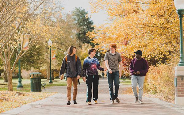四个学生在秋天走在人行道上