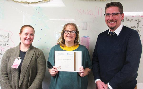 two members of faculty stand on either side of an Inside/Out program graduate proudly displaying her college readiness certificate