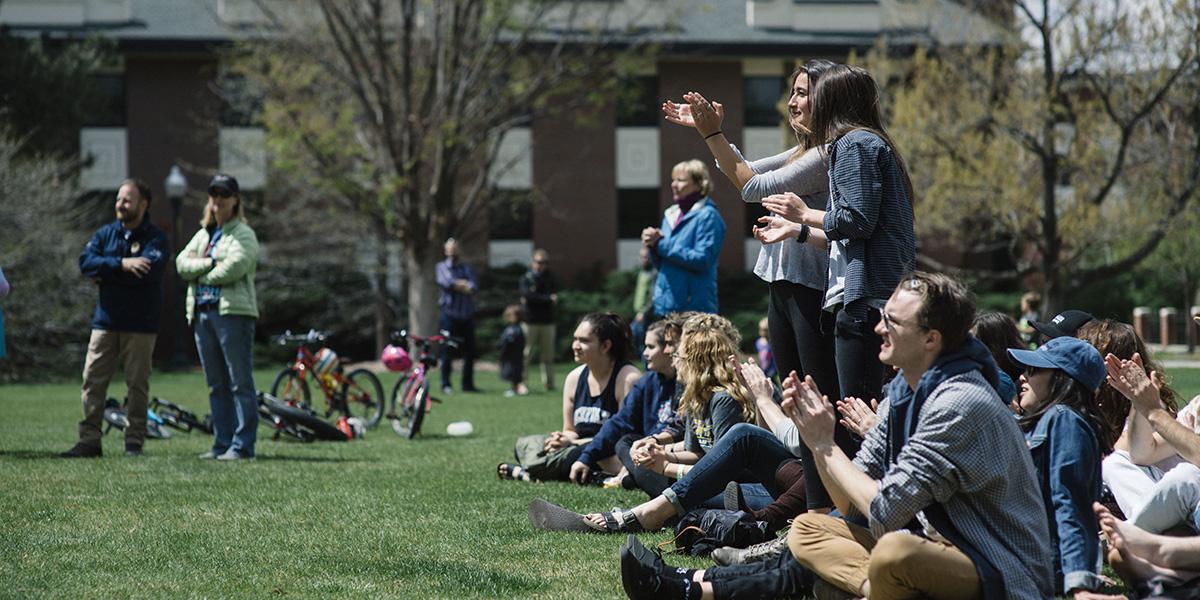 students sitting and clapping on the quad