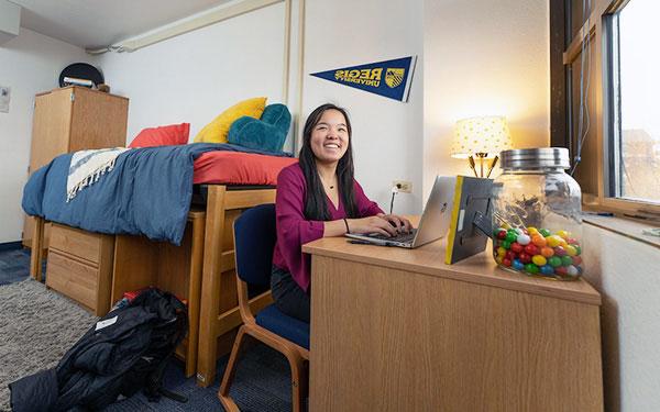 a student works on her laptop on the desk in her dorm room